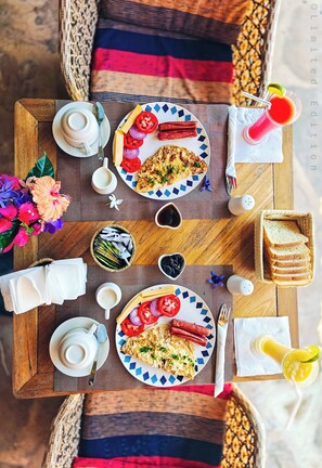 A wooden table with breakfast items including toast, eggs, sausages, and a drink. - Nungwi Roses Lodge (Nungwi)