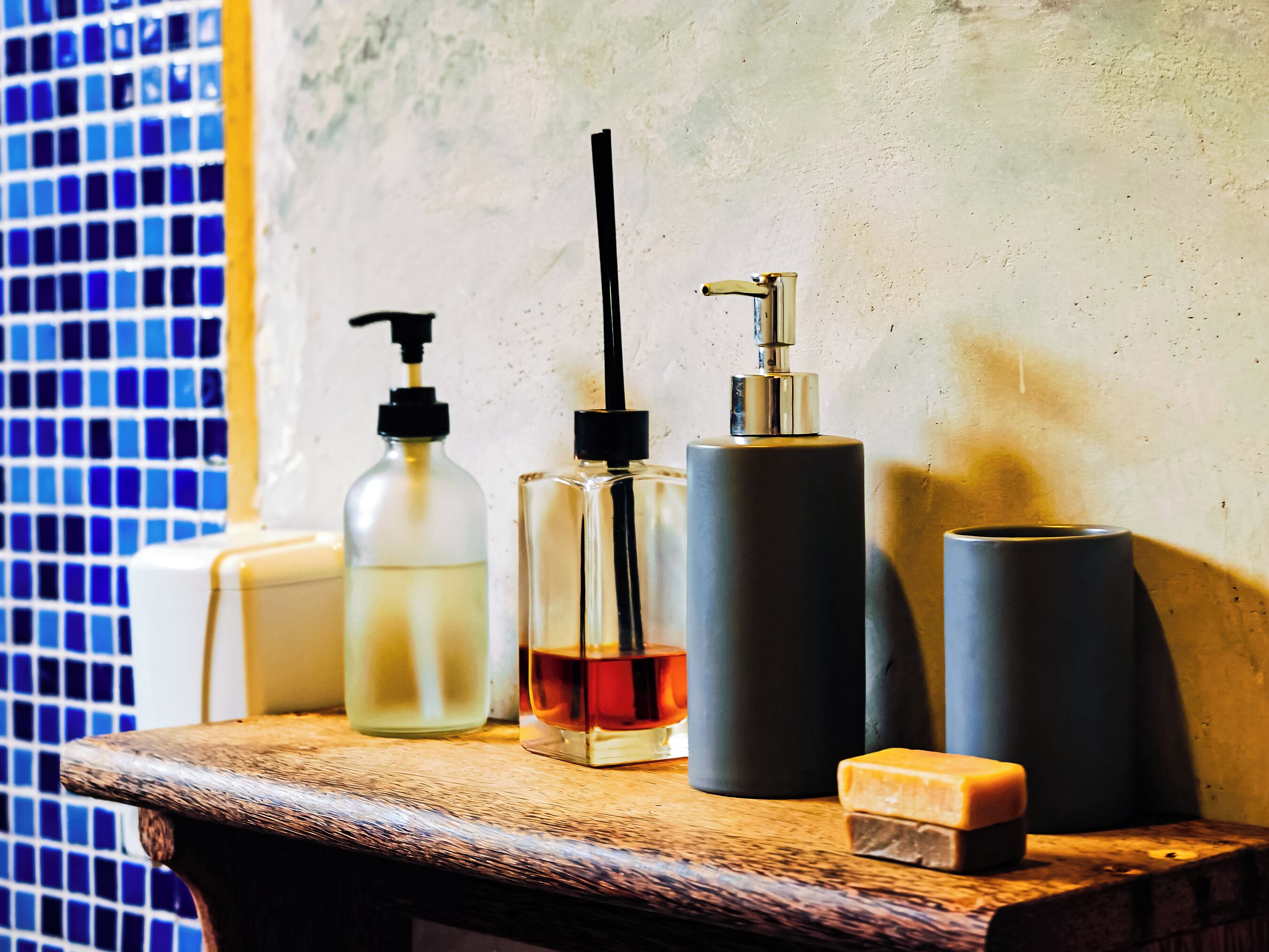 A bathroom counter with toiletries including a soap dispenser, a glass bottle, a cylindrical container, and a bar of soap.
