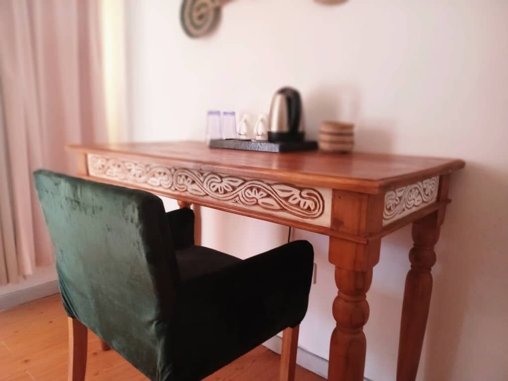 A wooden table with intricate carvings and a green velvet chair.