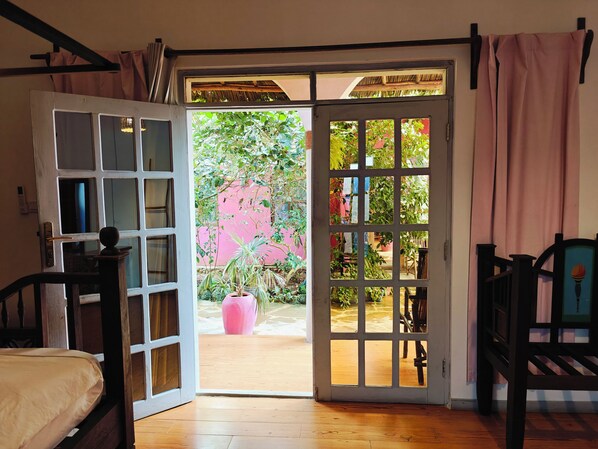 An open door leading to a garden with potted plants and a pink wall.
