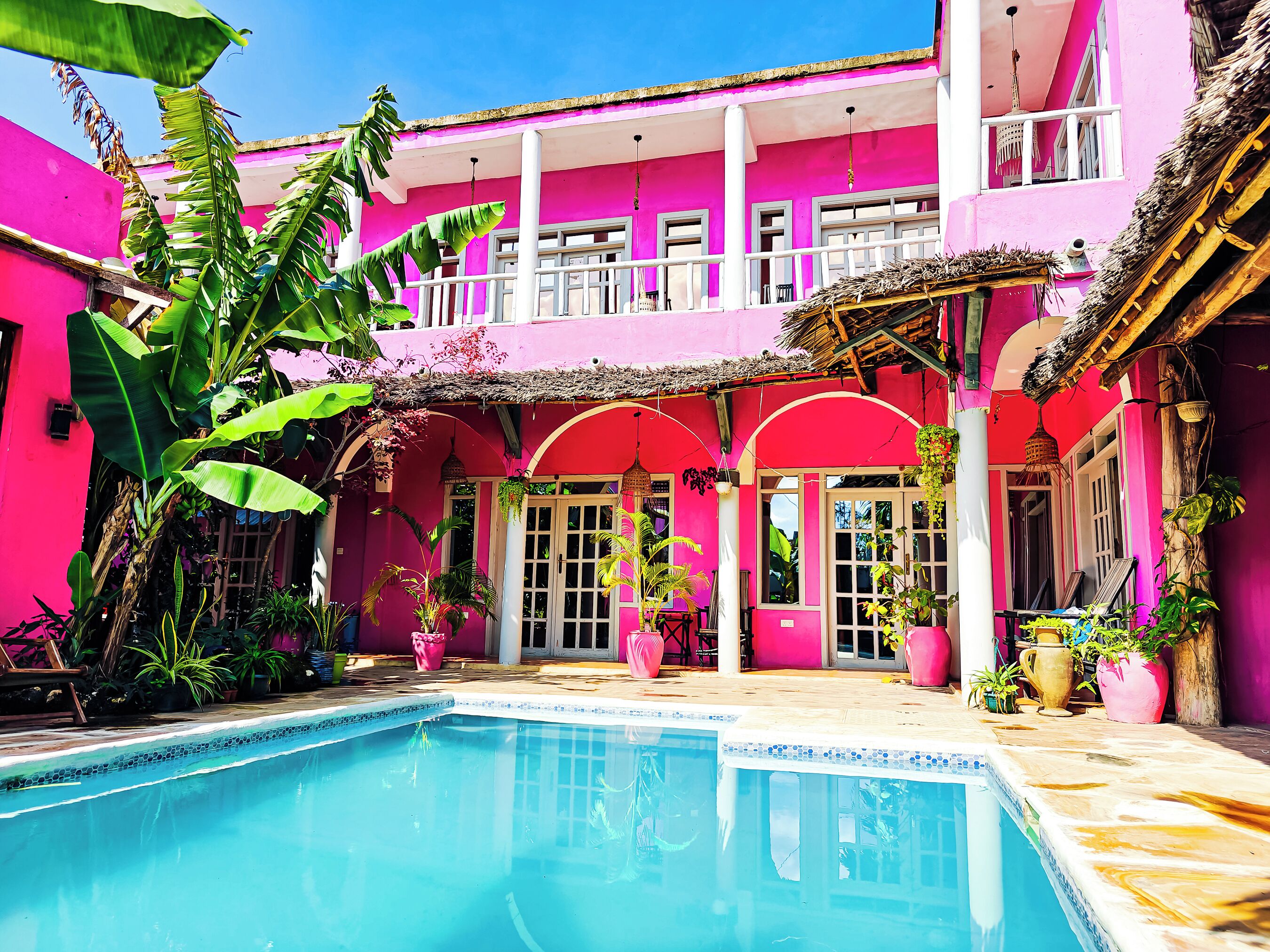Un bâtiment d’un rose vif, doté d’une piscine et agrémenté d’une végétation tropicale luxuriante.