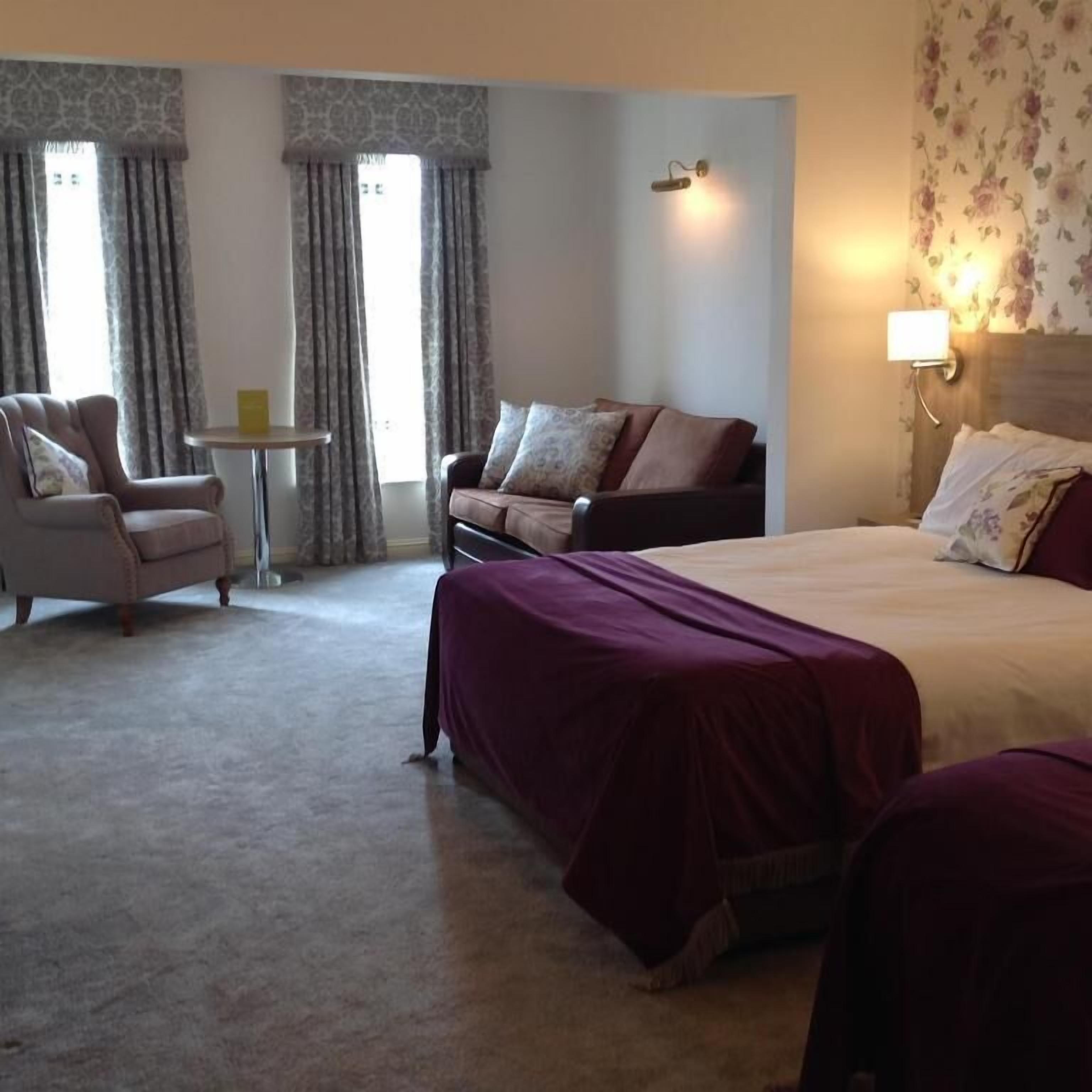 A hotel room with a large bed, a sofa, a chair, and a small table.