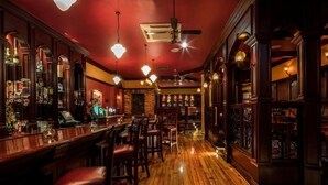 Un bar con pavimenti in legno e pareti rosse, con un bancone e sgabelli, e scaffali pieni di bottiglie.