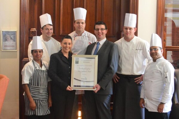 Un grupo de personas en un ambiente formal, algunas con gorro de chef, sosteniendo un certificado enmarcado.