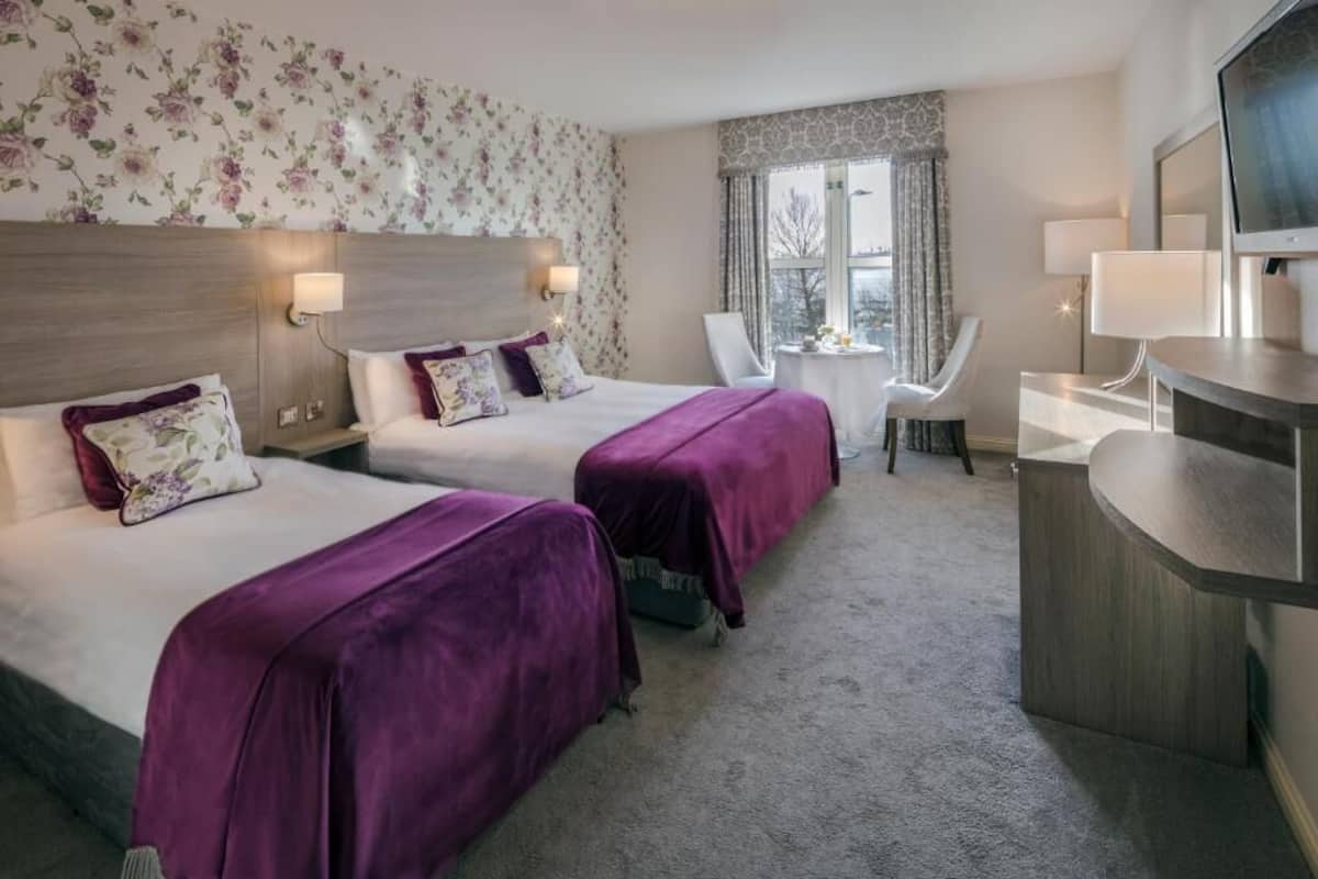 A hotel room with two beds, a desk, a chair, and a TV.