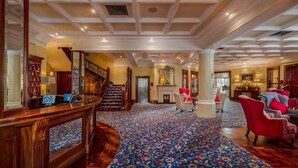 Un'ampia hall con una reception in legno, una scala e un tappeto decorato.