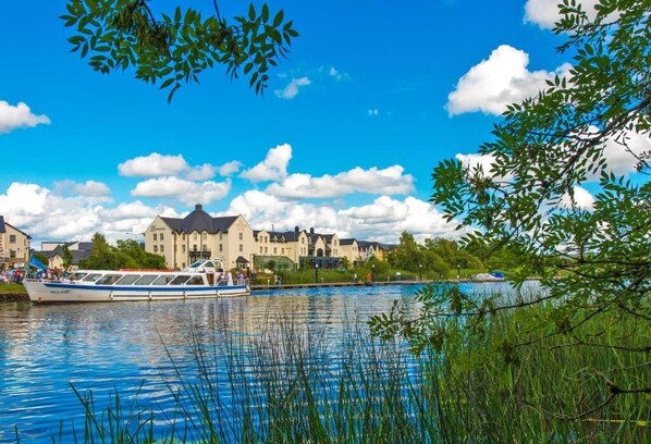 A river with a boat, buildings in the background, and greenery in the foreground. - The Landmark Hotel (Carrick-on-Shannon)