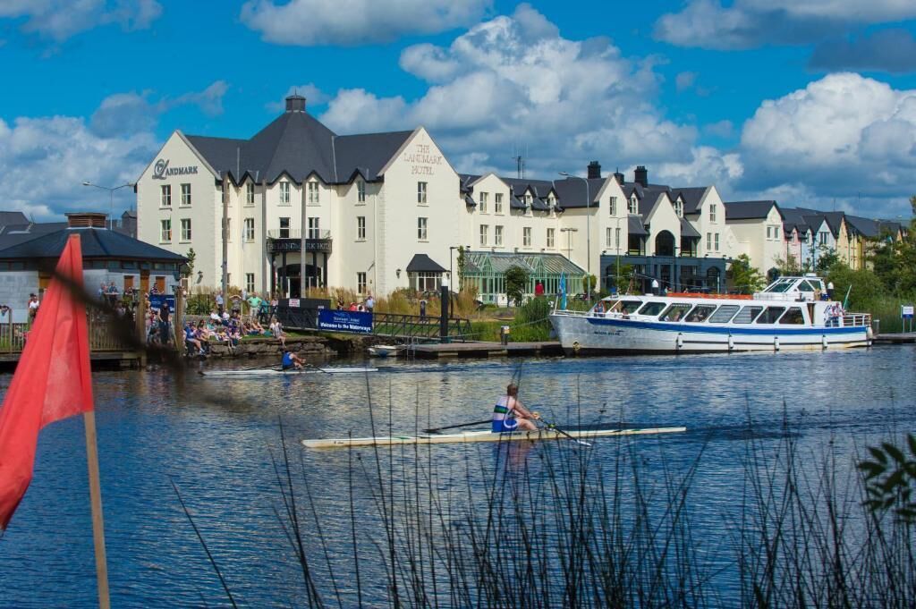 A waterfront hotel with a row of buildings, a boat docked at the pier, and a rower on the water.