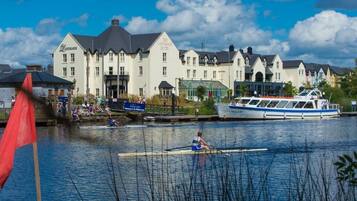 A waterfront hotel with a row of buildings, a boat docked at the pier, and a rower on the water.
