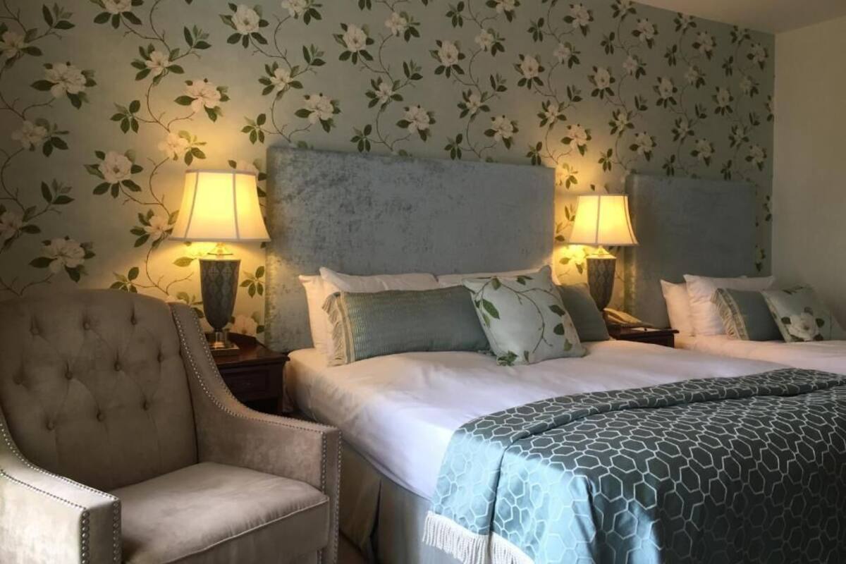 A hotel room with a large bed, two bedside tables with lamps, a chair, and floral wallpaper.