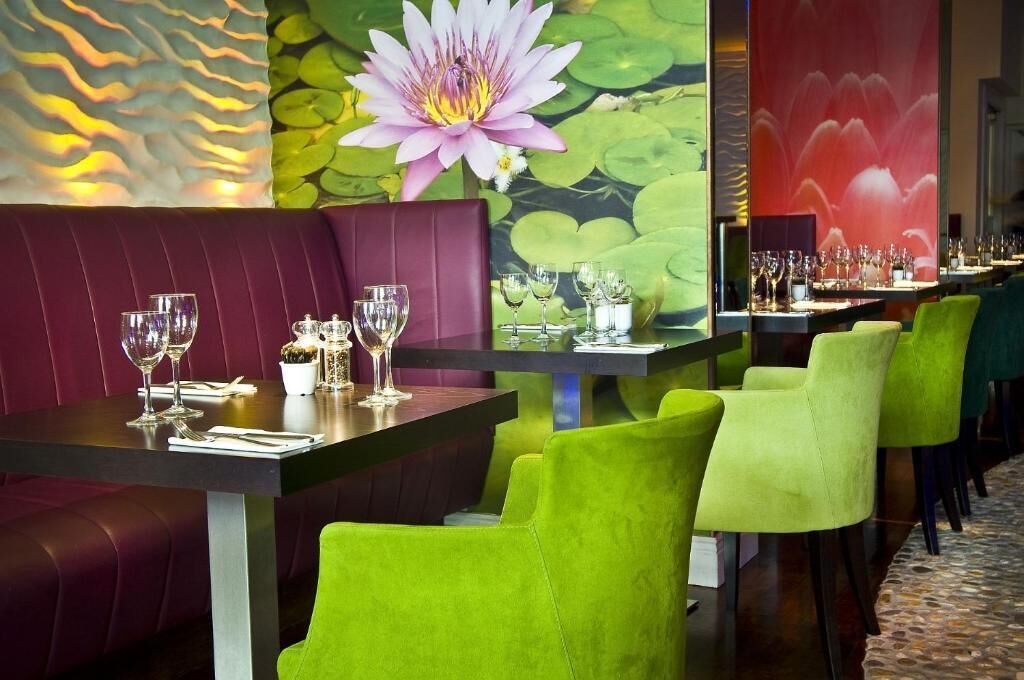 Un restaurante con una barra larga, sillas verdes y un gran mural de flores en la pared.