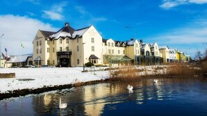 Un albergo con un grande edificio, uno stagno con cigni e un cielo azzurro limpido.