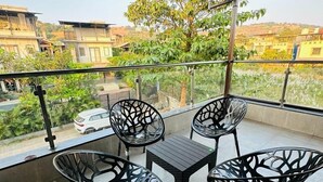 Ein Balkon mit vier schwarzen Stühlen und einem kleinen Tisch, mit Blick auf eine Wohngegend mit Häusern und Bäumen.