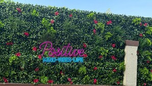 Ein Heckenbewuchs mit rosafarbenen Blüten und der Aufschrift "Positive Mind-Vibes-Life" in der Mitte.