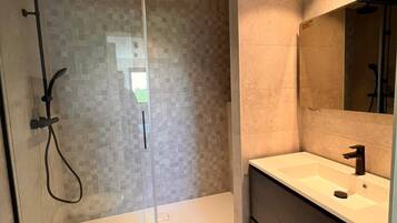 A modern bathroom with a glass-enclosed shower, a large mirror, and a wooden vanity.