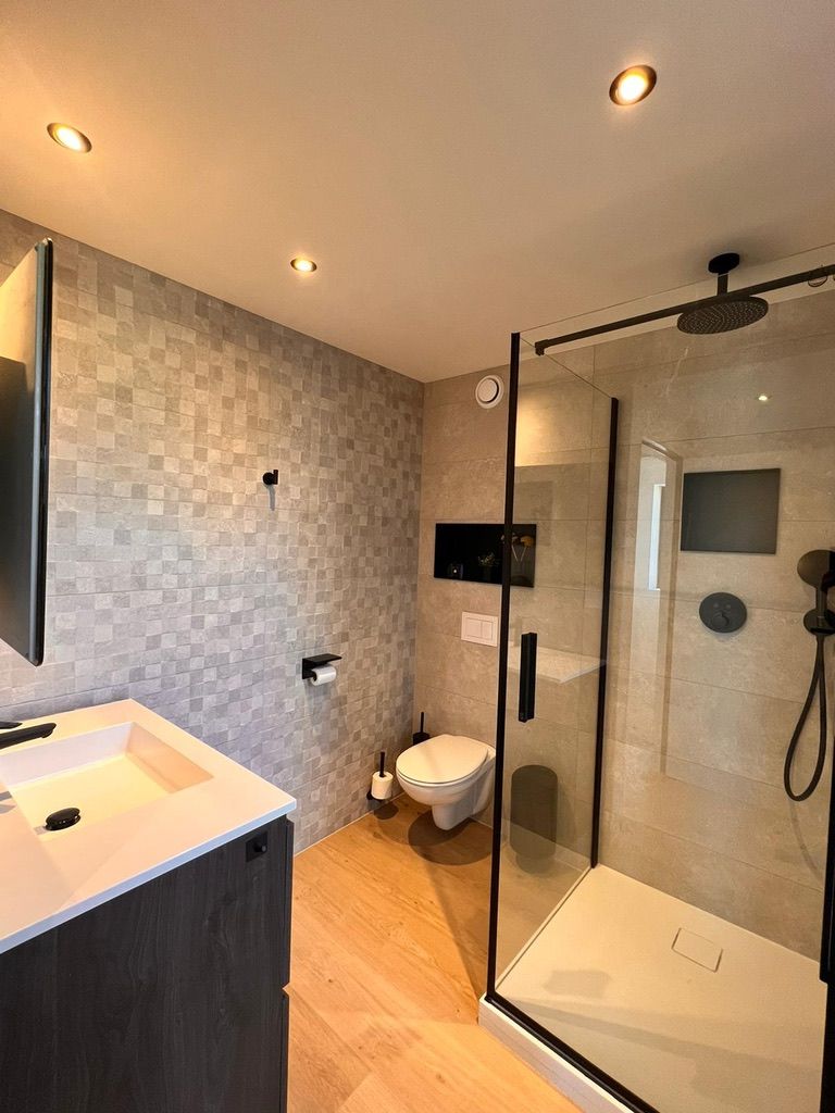 A modern bathroom with a glass-enclosed shower, a white sink, and a toilet.