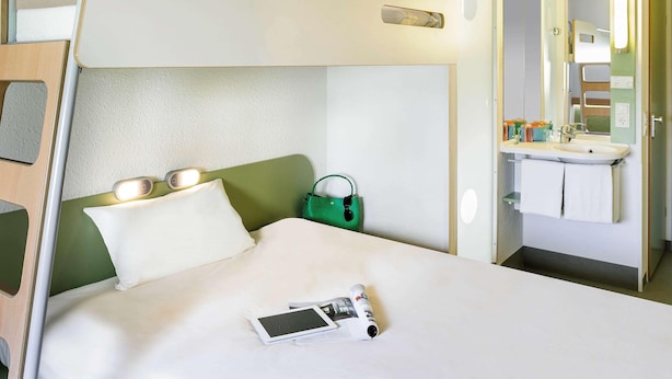 Un letto a castello con un comodino, una borsa verde e un tablet sul letto.
