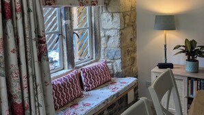 A cozy room with a stone wall, a bench with floral cushions, a table with chairs, a lamp, and a potted plant. - Newly Refurbished Cosy Cottage in the Heart of Chipping Campden (Chipping Campden)