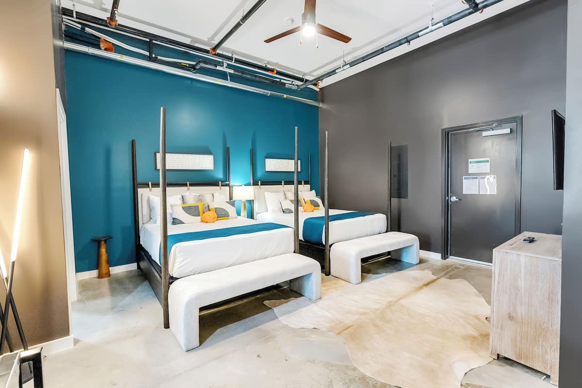 Quarto de hotel moderno com duas camas, um ventilador de teto e uma janela grande.
