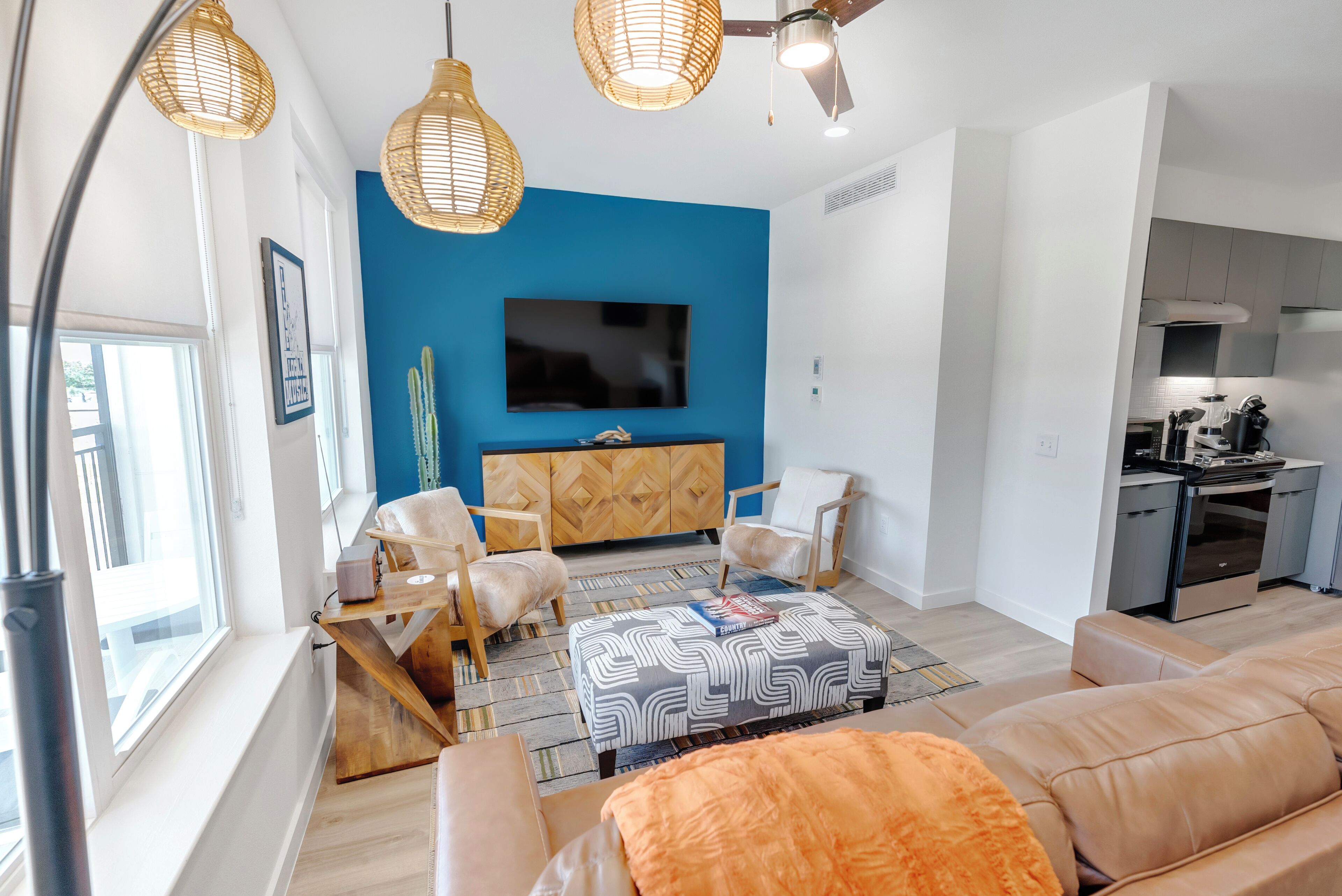 Una sala de estar moderna con una pared azul de acento, un televisor de pantalla plana, muebles de madera y una cocina con electrodomésticos.