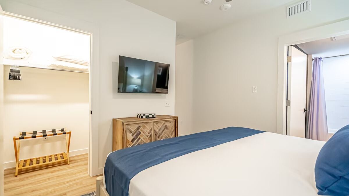 A hotel room with a bed, a TV mounted on the wall, a wooden cabinet, and a clothing rack.
