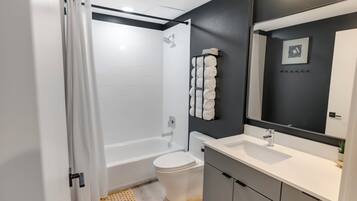 A modern bathroom with a white bathtub, a toilet, and a sink with a mirror.