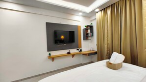 A modern hotel room with a flat-screen TV mounted on the wall, a wooden bedside table with a basket, and a large bed with a white comforter.