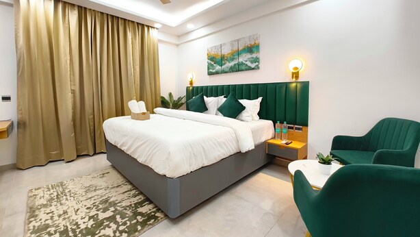 A modern hotel room with a large bed, green upholstered chairs, a ceiling fan, and a painting on the wall.