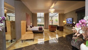 A spacious hotel lobby with a large bed, seating area, and a television. - Hotel Reyansh Pride (Palghar)