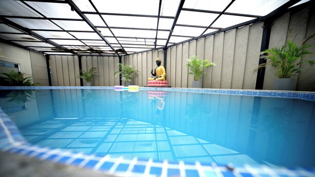 A swimming pool with a Buddha statue, potted plants, and a tiled floor.
