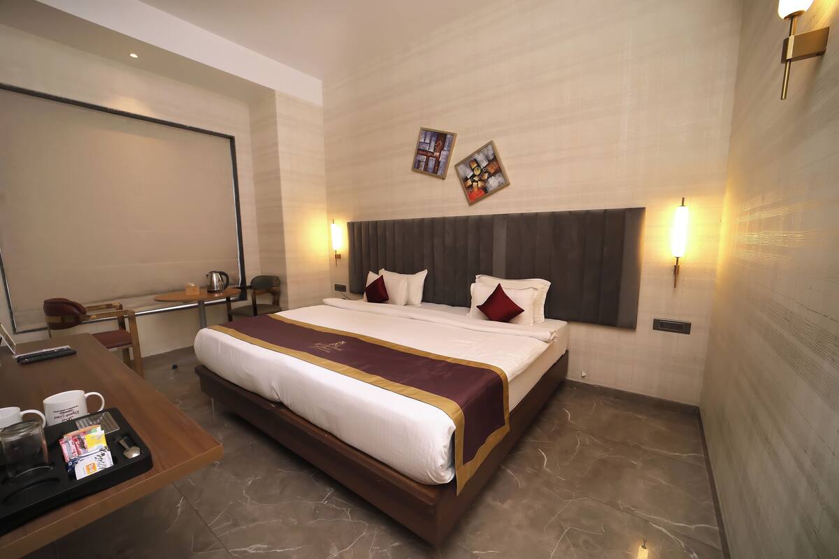 Habitación de hotel con una cama grande, un escritorio con cafetera y dos lámparas de pared.