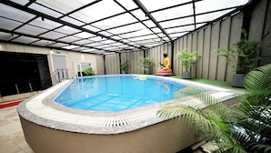 A hot tub with a tiled floor, surrounded by potted plants, and a covered area with a metal roof. - Hotel Reyansh Pride (Palghar)