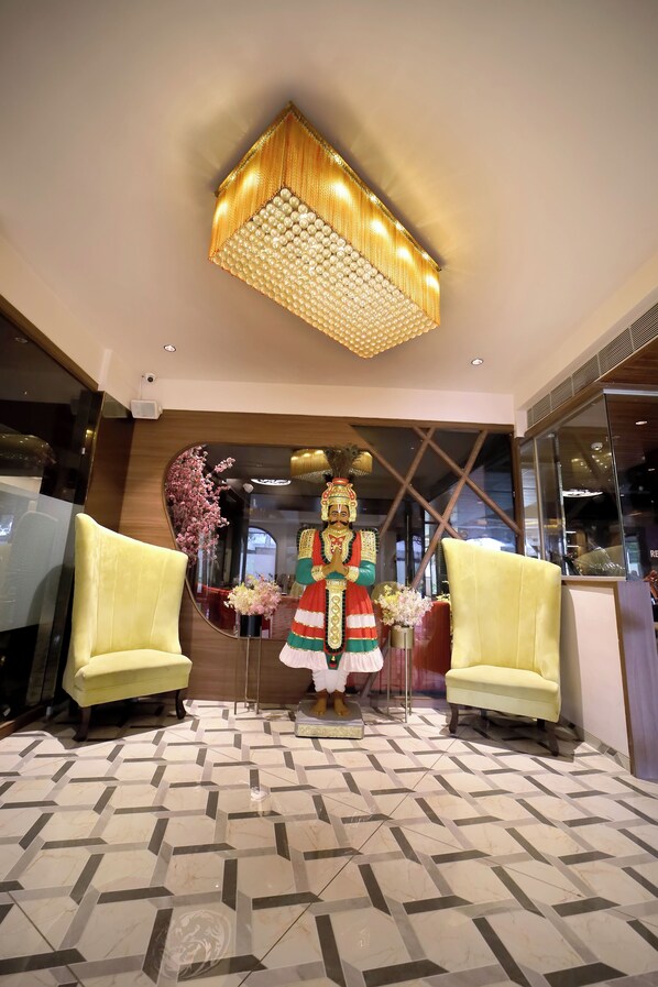A lobby with a large mirror, two yellow armchairs, a decorative statue, and a patterned floor.