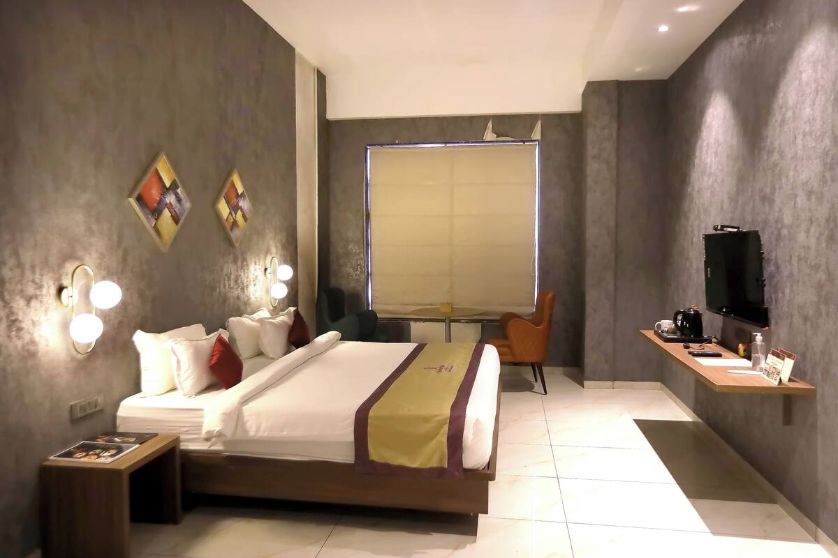 Habitación de hotel moderna con una cama grande, mesitas de noche, un escritorio con silla, televisión y obras de arte en las paredes.