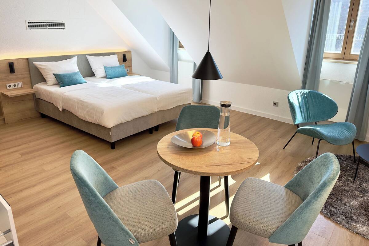Een moderne slaapkamer met een bed, nachtkastje, lamp en een zithoek met stoelen en een tafel.