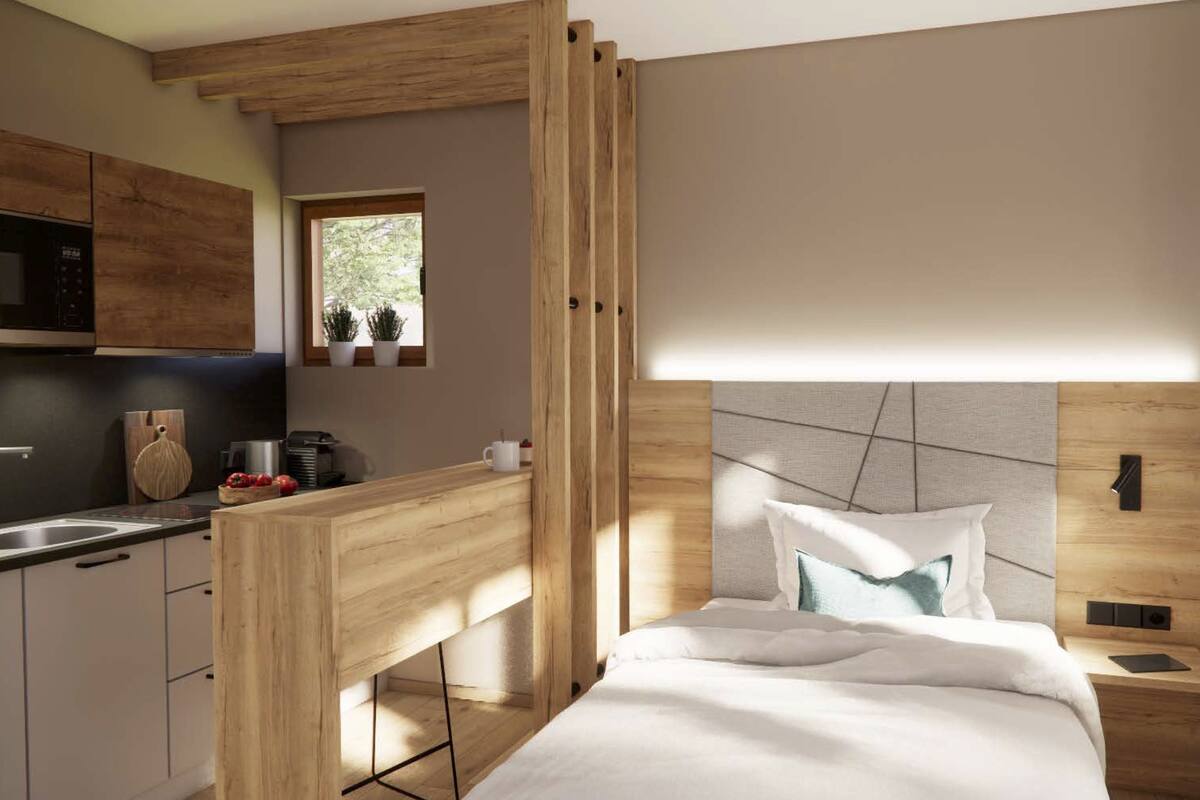 Een moderne slaapkamer met een groot bed, een houten bureau en een keukenhoek met een magnetron en kastjes.