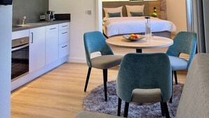Ein modernes Hotelzimmer mit Küchenzeile, einem Esstisch mit Stühlen und einem großen Bett mit Kopfteil.