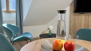 Ein moderner Essbereich mit einem runden Tisch, zwei Äpfeln, einem Glas und einer Vase mit Blumen.