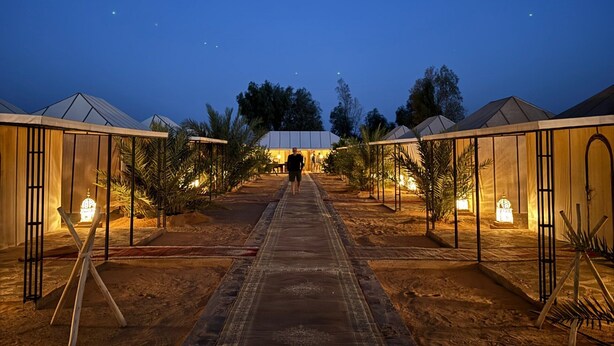 A pathway leading to a row of tents with a person walking towards them. - Sahara vibes luxury camp (Rissani)