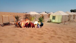 A desert setting with multiple tents and a small structure, likely a guesthouse, with a fire in the center. - Sahara vibes luxury camp (Rissani)