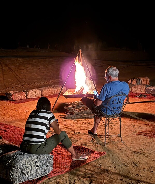 Deux personnes assises près d’un feu de camp, la nuit.