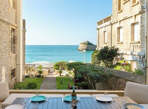 Un balcon avec une table dressée pour le dîner, offrant une vue sur la côte, avec une île rocheuse et un ciel dégagé.