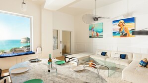 Ein modernes Wohnzimmer mit Glastisch, Sitzgruppe und Kunstwerken an den Wänden.