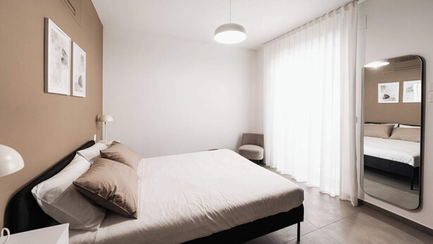 Ein modernes Schlafzimmer mit Bett, Stuhl, Spiegel und Pendelleuchte.