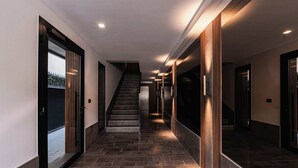 Ein modernes Interieur mit einer Treppe, die zu einer oberen Ebene führt, einem Flur mit Fliesenboden und einer Tür mit Blick auf einen Zaun.