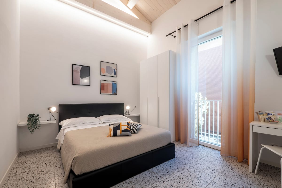 A modern bedroom with a bed, a desk, and a balcony.