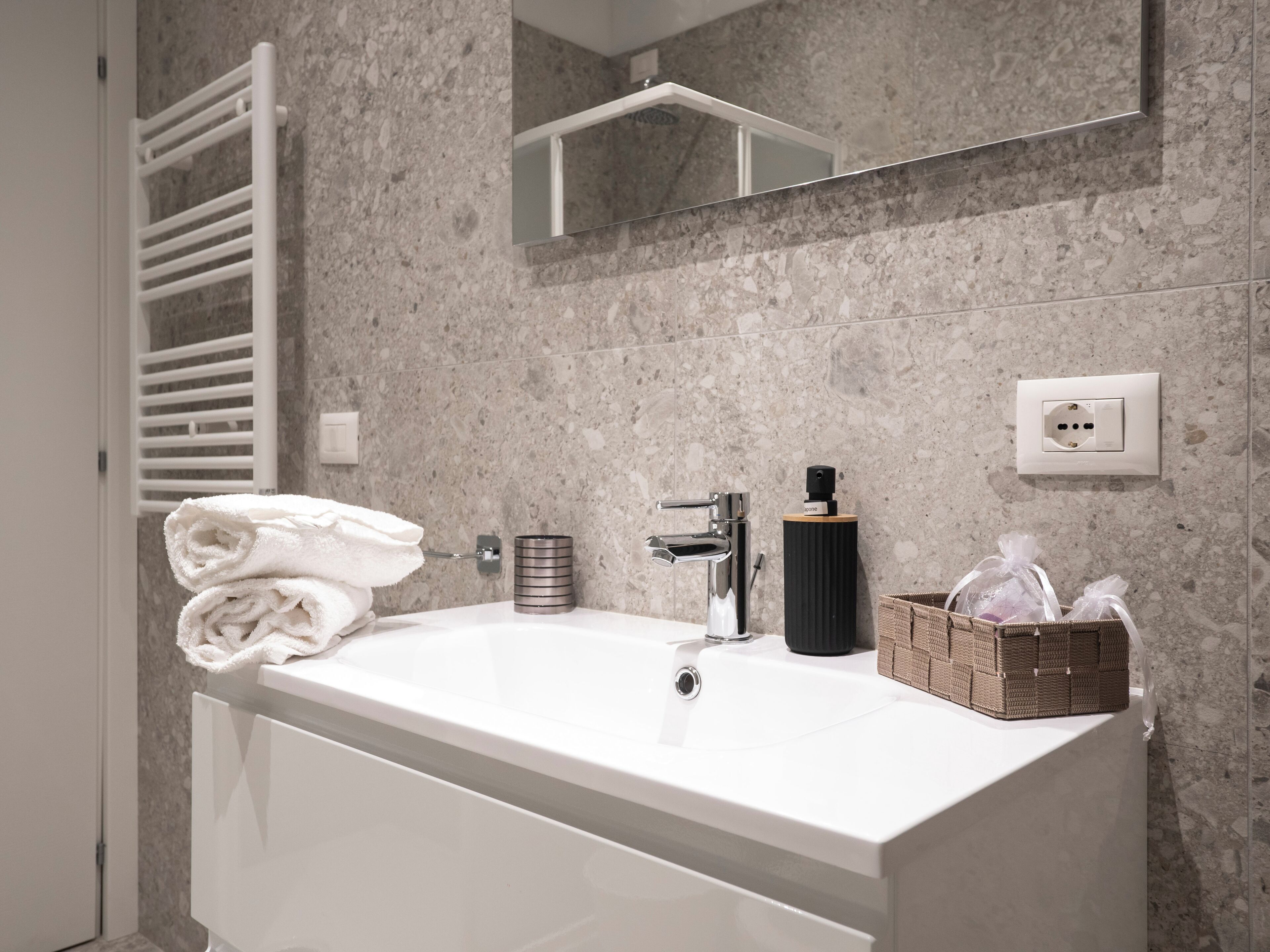 Une salle de bain moderne avec une baignoire blanche, un porte-serviettes, un miroir et un panier contenant des articles de toilette.