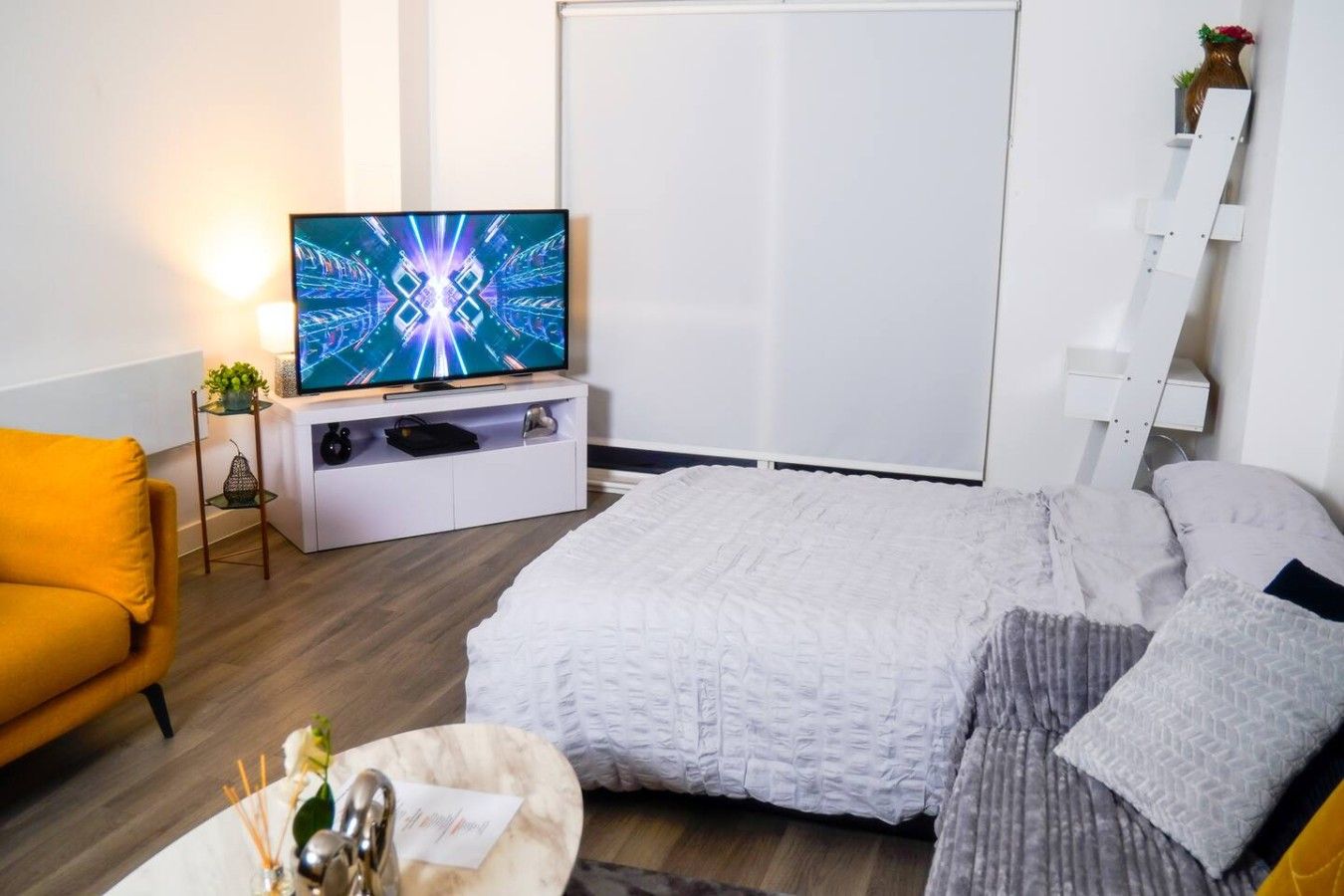 Une chambre à coucher moderne avec un lit, un téléviseur posé sur un meuble, une chaise et une table de chevet.