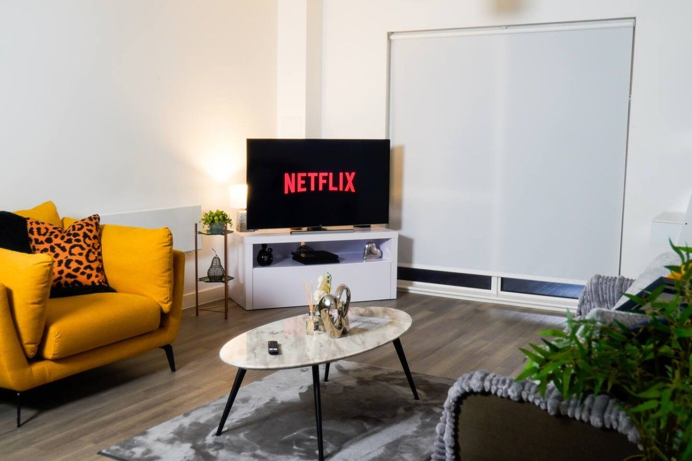 A living room with a sofa, a coffee table, a television displaying 'NETFLIX', and a whiteboard.