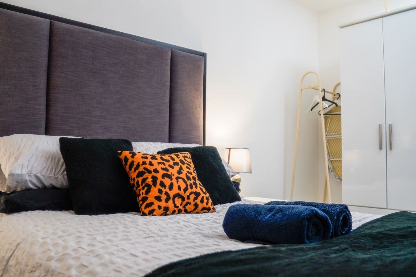 A neatly made bed with a headboard, a lamp, and a wardrobe.